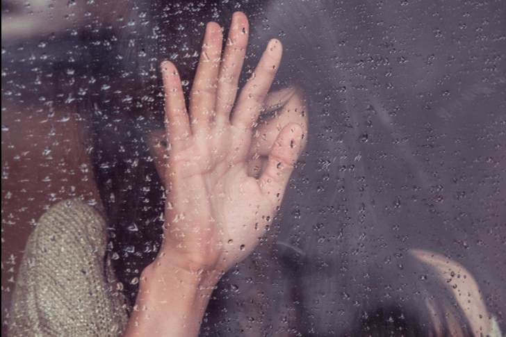 雨の日の窓に寄りかかる女性