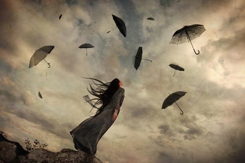 空に舞う黒い傘を見上げる女性