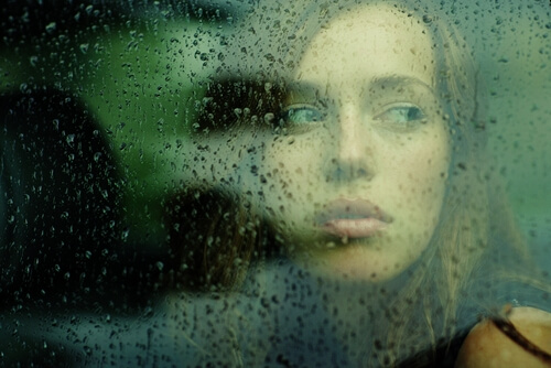 雨の窓の外を眺める女性