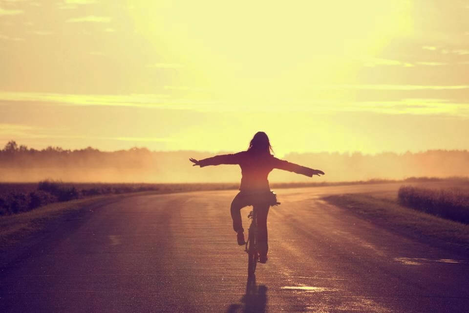 自転車を手放し運転する女性と夕日