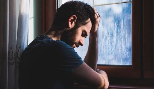 窓の前で悲しむ男性